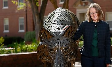 Katie Homar standing next to one of the copper wolf statues on NC State's campus