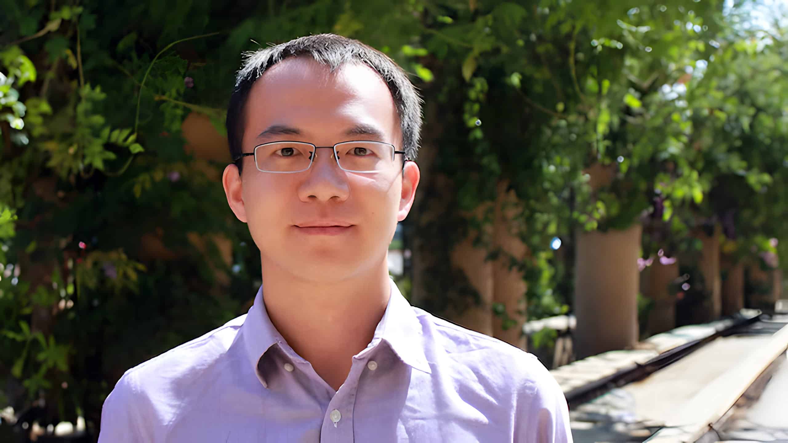 A headshot of Chao Chen standing outside in front of some trees.