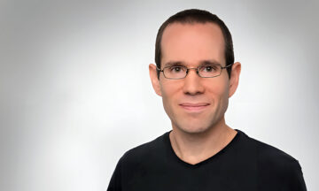 A headshot of Itai Gurvich standing in front of a white background.