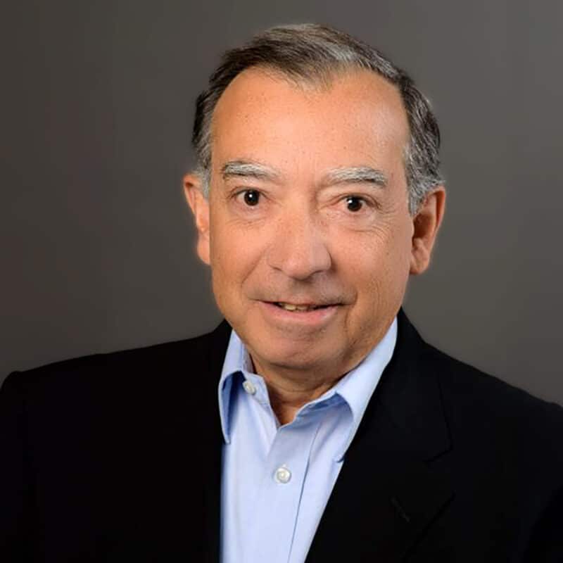 A headshot of Jorge Nocedal standing in front of a gray background.