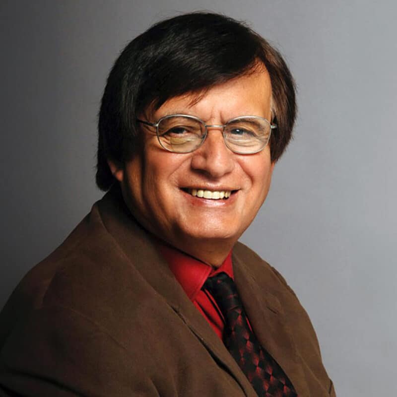 A headshot of Richard Tapia standing in front of a gray background.