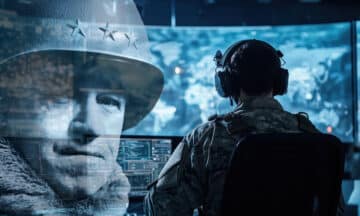 A military fellow standing in front of several computer monitors doing research